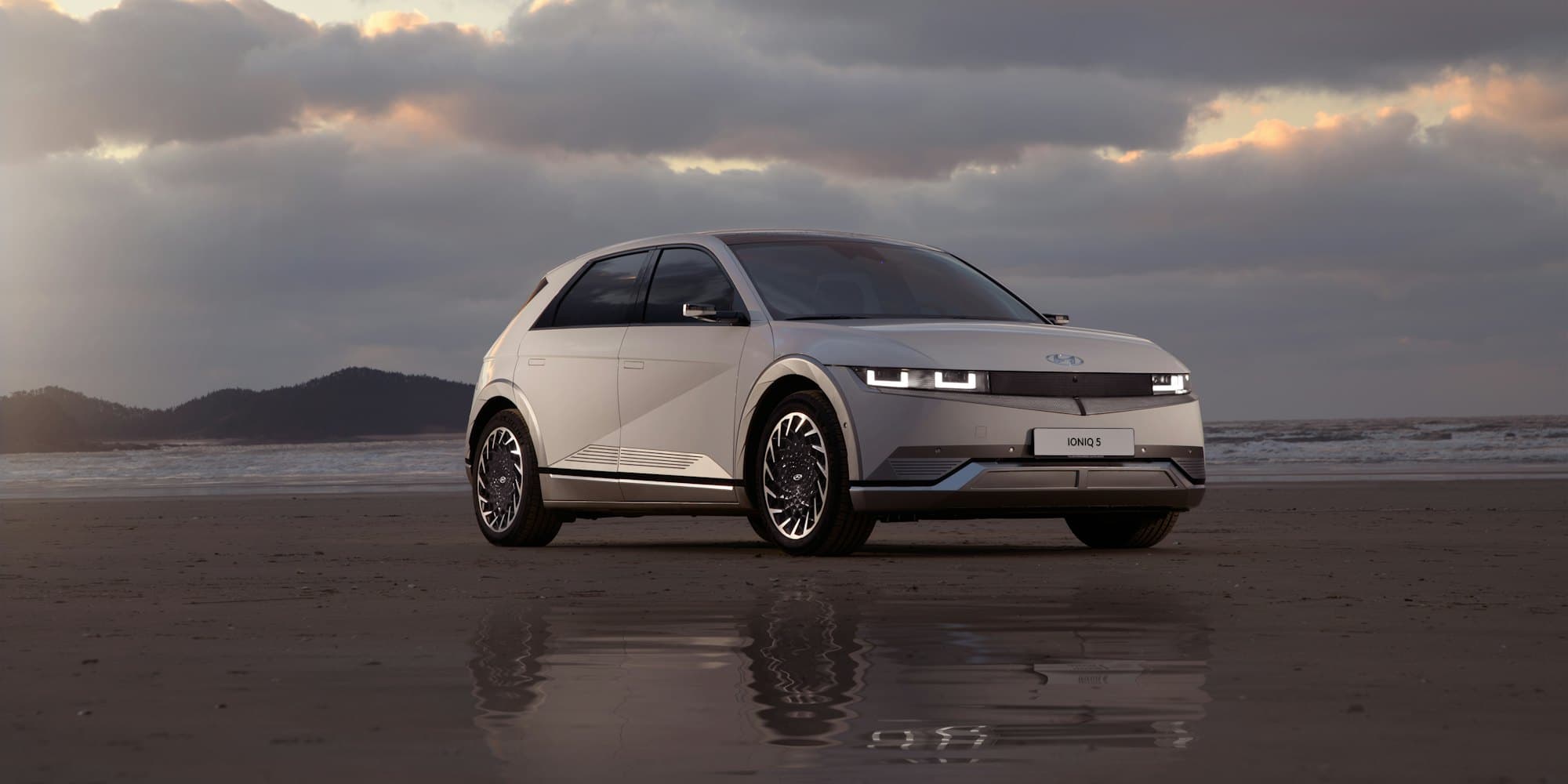 Hyundai Ioniq 5 electric crossover parked on a wet beach under a dramatic sunset sky