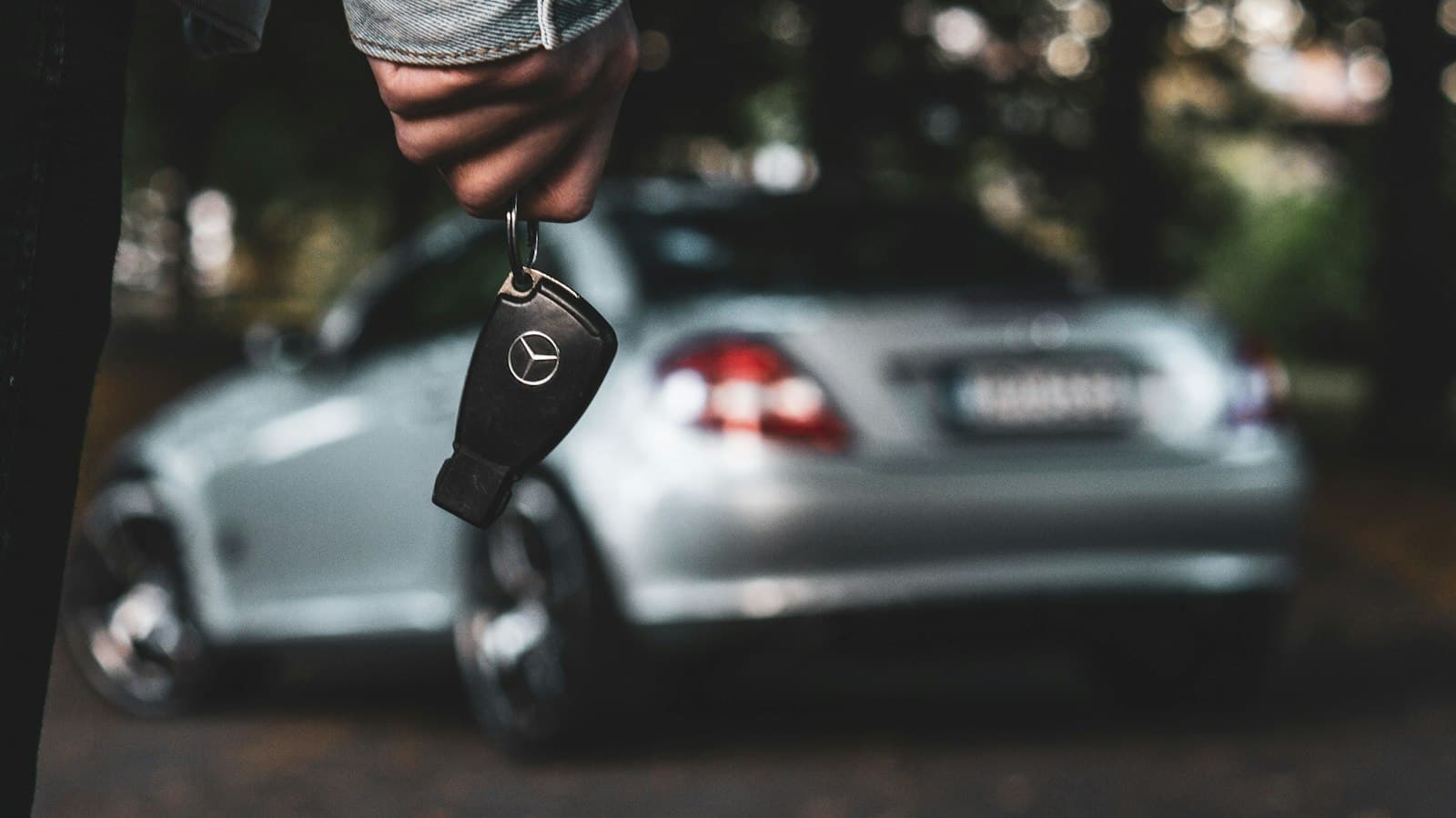 Driver holding a car key in front of a silver sedan
